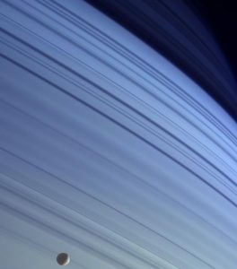 Pohľad zo sondy Cassini na severnú pologuľu Saturna, kde je zreteľná modrá farba planéty spôsobená rozptylom slnečného svetla v horných vrstvách atmosféry. Tmavé pruhy sú tiene prstencov, mesiac na okraji fotografie je Mimas.